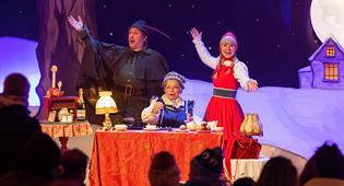 Efteling characters Little Red Riding Hood, Grandmother and the Hunter play bingo on a warmly lit stage.